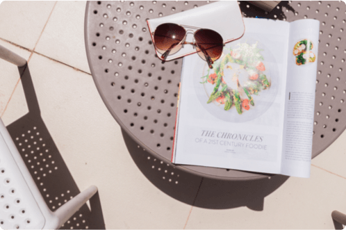 On the balcony table of St. Blue Bay, there is a sunglass and a food magazine