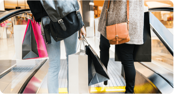 Two ladies on an escalator are carrying bags after shopping.