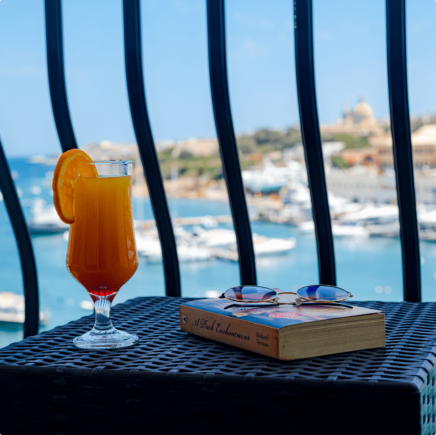 an image of a glass of orange juice and a book on a table in the balcony at St Hotel room