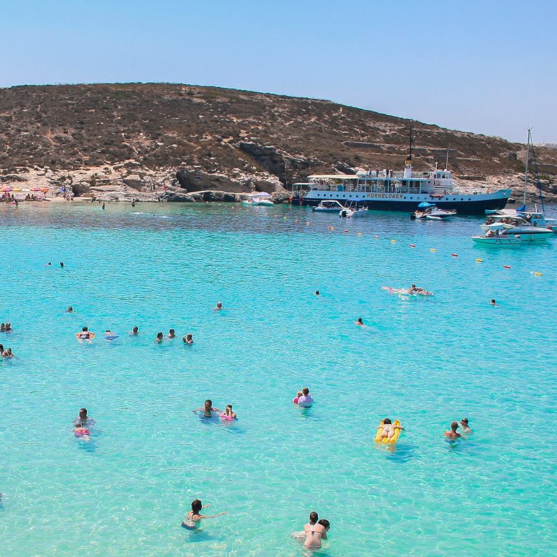 an image of people who swimming in the beautiful water in Comino island in Malta that shows tourism attractions to tourists who stay at ST hotels